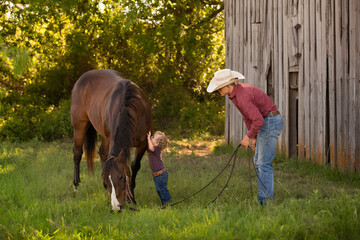 Child kissing horse with father standing nearby on pasture land near an old barn on a cattle ranch