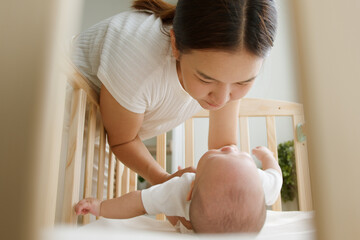 Young Asian mother carry up her newborn baby from crib