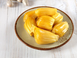Already peeled Fresh and sweet prime jackfruit or nangka in Indonesian served on a plate with its edible seeds on the background. 
