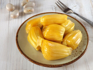 Already peeled Fresh and sweet prime jackfruit or nangka in Indonesian served on a plate with its edible seeds on the background. 