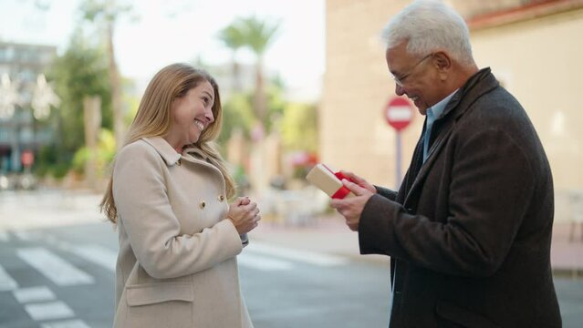 Middle age couple couple hugging each other holding birthday gift at street
