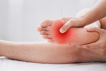 Pain in the foot, Man holds hands to his feet, foot massage, cramp, muscular spasm, red accent on the foot, close-up.