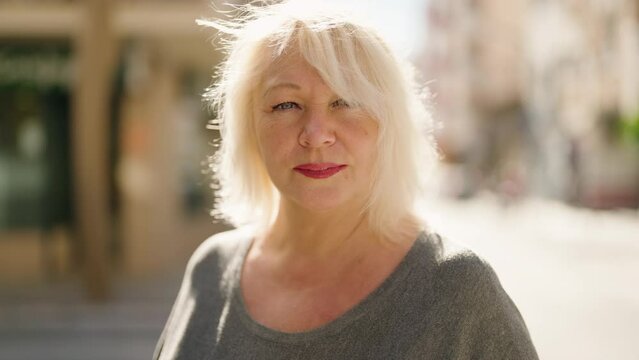 Middle age blonde woman with relaxed expression standing at street