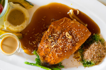 salmon fish steak grill in fried onions and white sesame with mashed potatoes and pumpkin combine to sauce and tomato on dish with salad and top view for seafood and omega 3 in japanese restaurant