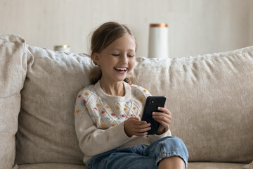 Happy laughing gen Z little girl kid talking on video call on smartphone on couch at home, using...