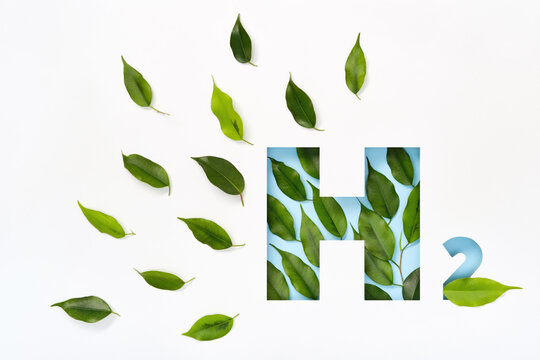 H2 hydrogen icon made of cut paper and green leaves on blue background. Emission-free biofuels concept