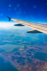 View from the airplane window at a beautiful blue clear sky, earth, sea and the airplane wing