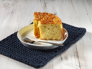 Sliced moist cheese chiffon sponge cake served in white plate on crochet place mat over the white wooden background. Copy space available.