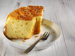 Sliced moist cheese chiffon sponge cake served in white plate on crochet place mat over the white wooden background. Copy space available.