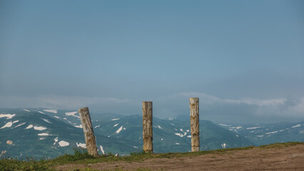 Old wooden totem poles stand on the hillside. Background - blue sky, mountain range. Copy space. Kamchatka. Vilyuchinsky Pass