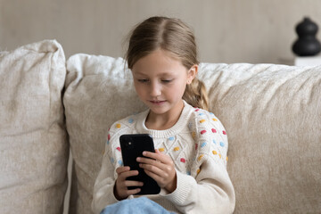 Digital addicted kid engaged in smartphone using, watching media on mobile phone at home, reading,...