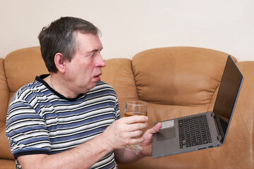 A man with a surprised face holds a laptop in his hands while sitting on couch - 488287934