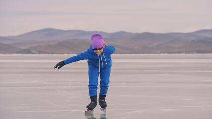 The child train on ice professional speed skating. The girl skates in the winter in sportswear, sport glasses, suit. Children speed skating short long track, kid sport. Outdoor slow motion.