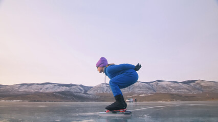 The child train on ice speed skating. The athlete at the start, in a sports stance. The kid girl skates in the winter in sportswear, sport glasses. Children speed skating short long track. Outdoor.