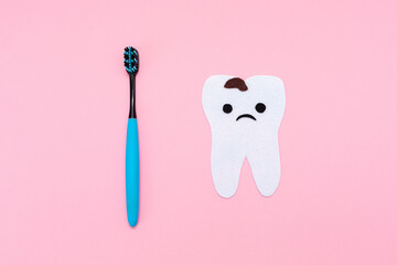 A plastic toothbrush and a felt-cut out sad tooth with decay. Flat lay. Pink background. Concept of the oral cavity