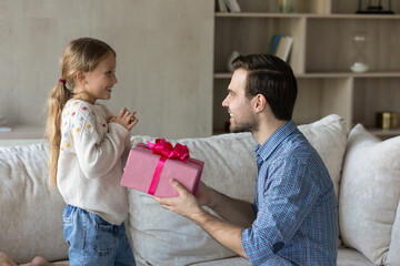 Happy loving dad giving surprise gift to excited little daughter kid, holding pink wrap,...