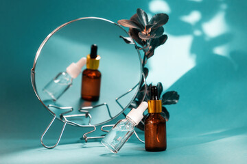 Close up of two glass bottle of cosmetic on turquoise background with mirror and leaves. Concept of herbal organic beauty products