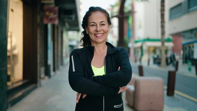 Middle age woman wearing sportswear smiling confident standing with arms crossed gesture at street