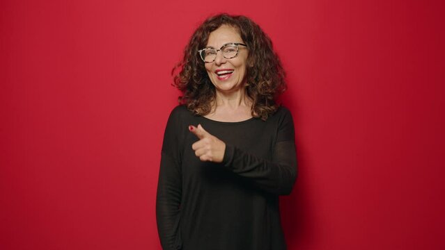 Middle age woman smiling confident pointing with finger over red background