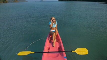 Pretty slim woman in elegant swimsuit lies in pink plastic kayak drifting on azure ocean at exotic resort upper view. Traveling to tropical countries. Girl is sailing on kayak in ocean, view above.