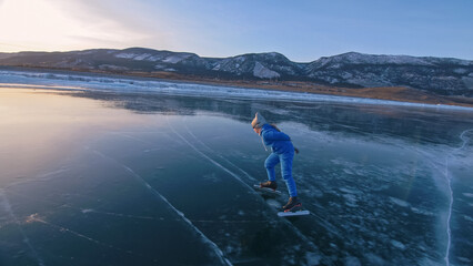 Naklejka premium The girl train on ice speed skating. The child skates in the winter in blue sportswear suit, sport glasses. Children speed skating sport. Outdoor slow motion. Snow capped mountains, beautiful ice.