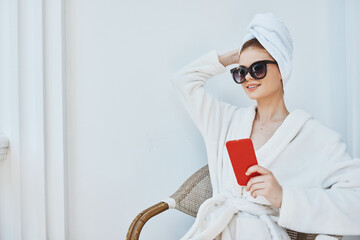 woman in sunglasses with a red phone sits on the balcony