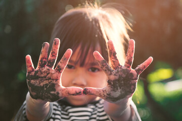 Cute little girl smiles and shows off her muddy hands while planting trees in the backyard....