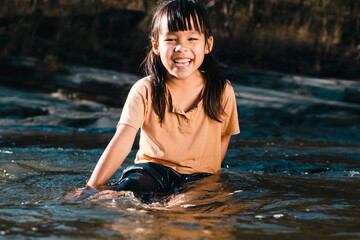 Asian little girl playing in the forest stream. Active recreation with children on river in summer.