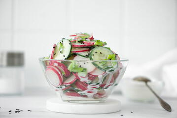 vegetable salad of cucumbers and radishes with sour cream and sesame seeds in a glass bowl