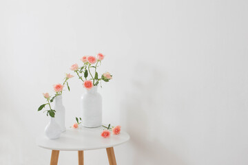 pink roses in white vase on  table on background white wall