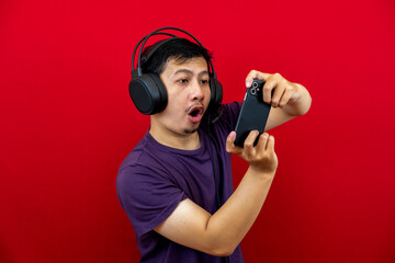 An asian man is playing a game on his smartphone and wearing a headset.