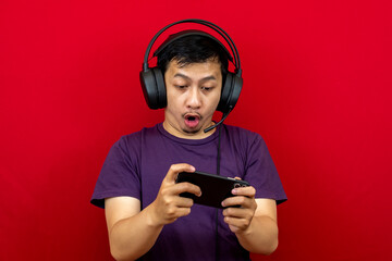 An asian man is playing a game on his smartphone and wearing a headset.