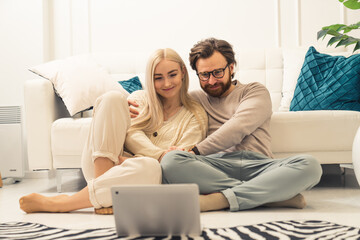 Obraz premium caucasian blonde long-haired beauty sitting on the floor with her affectionate partner and watching videos on their laptop. High quality photo