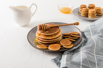homemade pancakes and mini pancakes on a grey plate are served with honey. cream or milk, a bowl of honey to improve the taste.