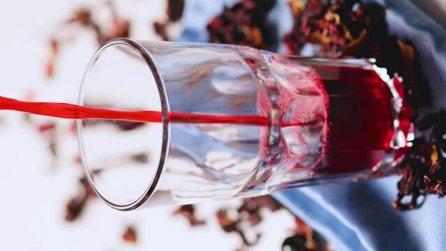 Hibiscus tea pouring into a glass. Hibiscus leaves for making trendy tea. Red hibiscus tea on a blue napkin. Vertical video