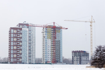 High-rise buildings under construction with red and yellow building cranes under falling snow in winter day