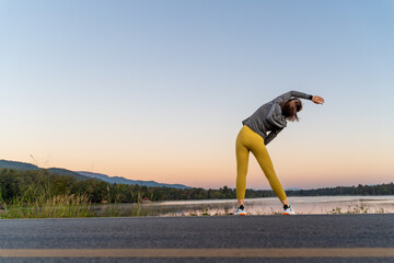 Back view of a woman stretching her arms and legs before her early morning exercise at a local lake park