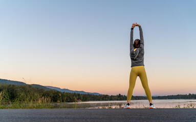 Back view of a woman stretching her arms and legs before her early morning exercise at a local lake...