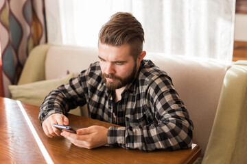 Young hipster guy looking news from social networks read via smartphone on free time in cafe