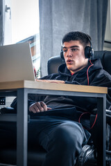 A young male athlete sits in front of a laptop in his room.