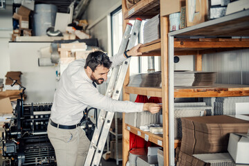 A manager looking for graphic material at printing shop while standing on ladders.