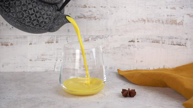 Turmeric golden moon milk is poured from a teapot into a glass. Healthy drink.