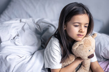 Sleepy little girl with her favorite teddy bear in bed in the morning.