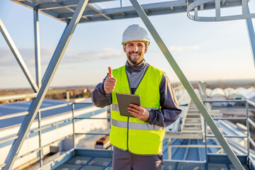 A happy industry worker standing on top of the silo with tablet in hands and giving thumbs up of supply. © Dusan Petkovic