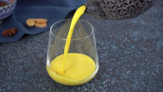 Turmeric golden moon milk is poured from a teapot into a glass. Healthy drink.