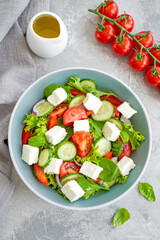 Salad with fresh vegetables and cheese in a bowl on a concrete background. Greek salad, vegetarian dish. Top view.
