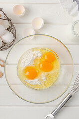 Cooking dough for traditional thin pancakes or crepes. Eggs, flour, salt, sugar in a bowl on a white wooden background. Recipe step by step. Food for Maslenitsa.