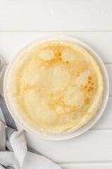 Stack of traditional thin pancakes or crepes on a plate with honey and sour cream on a white wooden background. Food for Maslenitsa. Copy space.