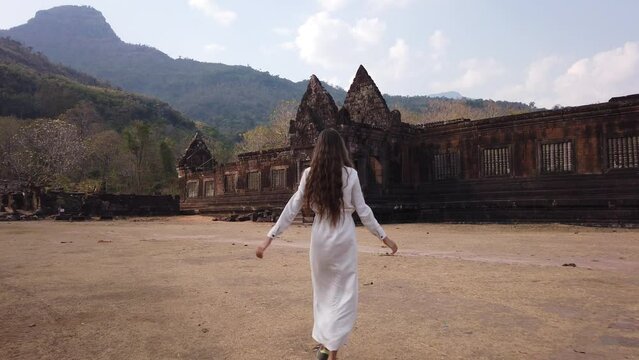 Young beautiful woman walking near ancient palaces in Vat Pou Khmer Hindu Temple located at the base of Phu Kao mountain. Traveling in Laos, Champassak province. Slow motion. Ancient culture religious