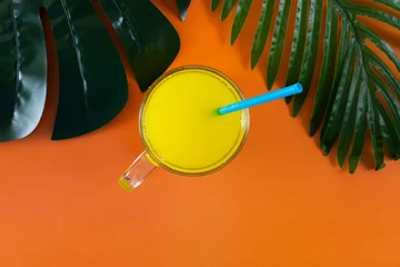 Tuinposter a glass glass with orange juice on an orange background, a concept of summer and relaxation © Dmitry